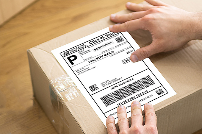 A Click-N-Ship label being placed on a package that sits on a desk.
